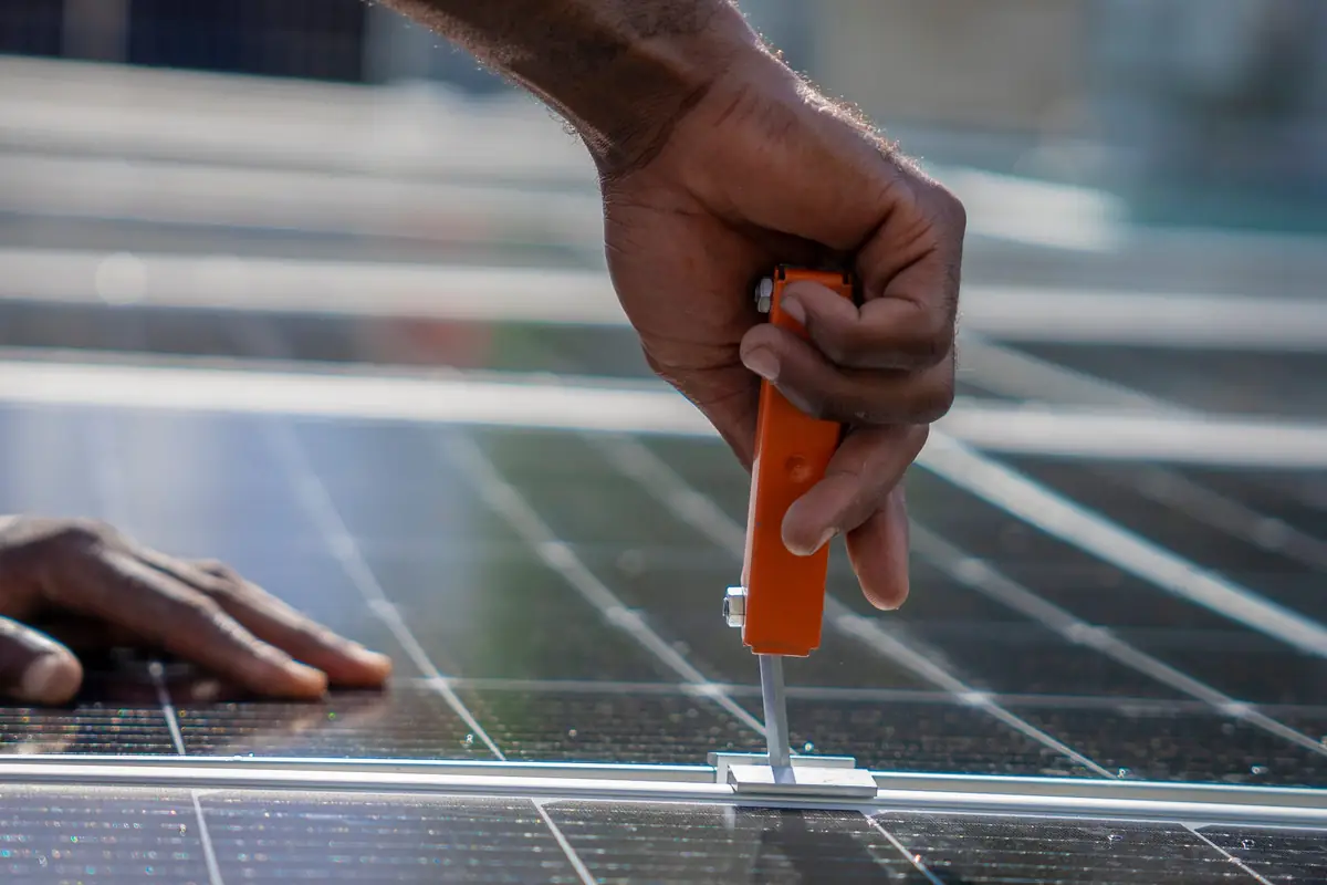 Close-up of an installer's hand tightening a clamp between two solar panels