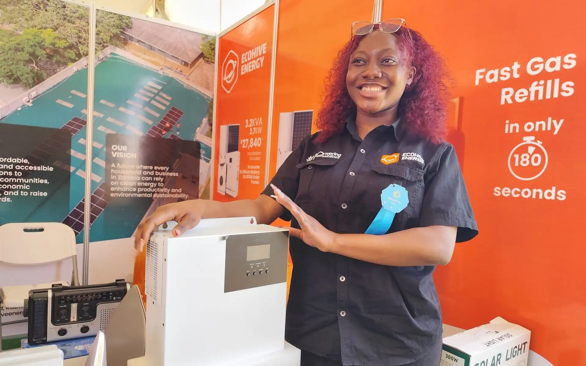 A smiling EcoHive team member presenting a home inverter at the EcoHive stand