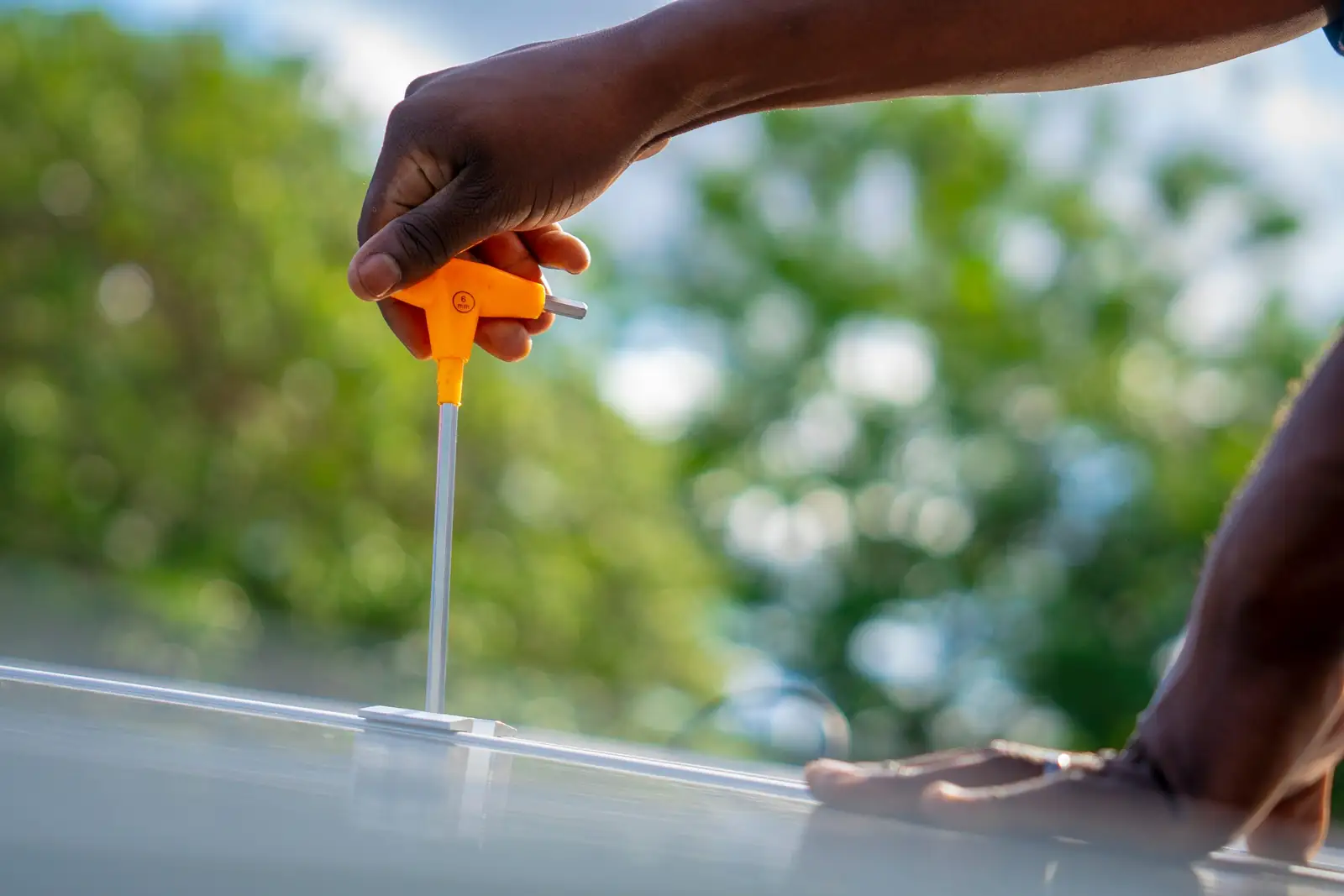 Close-up of an installer tightening a solar panel clamp, trees softly blurred behind