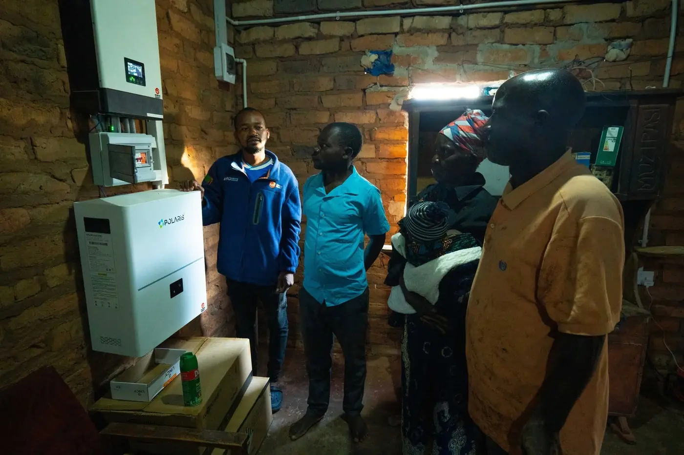 Residents and an EcoHive technician beside a newly installed inverter and battery